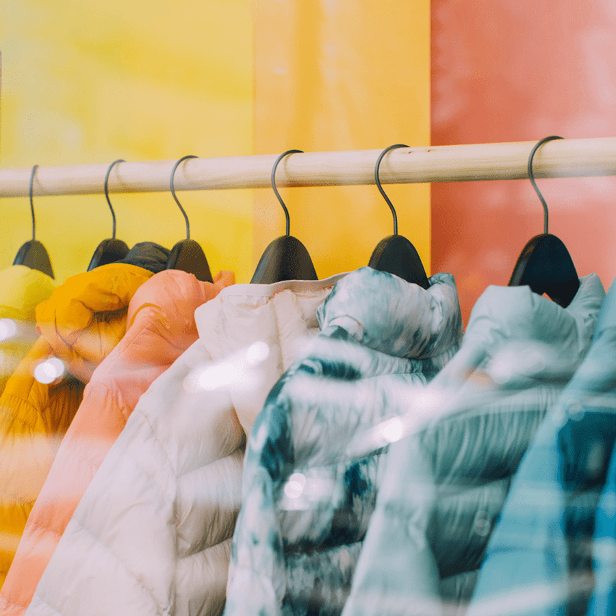 A row of colorful puffer jackets hanging on a display rack against a bright background.