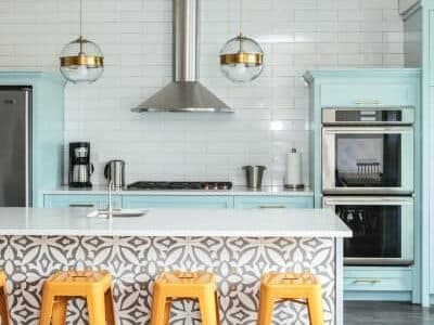 A modern kitchen featuring turquoise cabinetry, patterned backsplash, and yellow bar stools.
